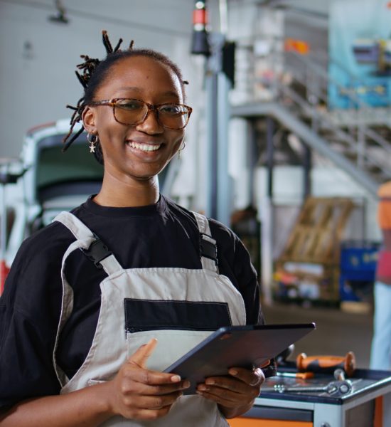 Certified repairman in auto repair shop showing customer what needs to be changed on her car for it to properly work. Garage expert inspecting vehicle placed on overhead lift, talking with woman